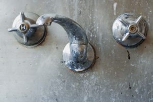 close up of a tap set set in a stainless steel sink or trough. Colorfully grungy and disgusting.