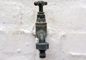 Outdoor faucet on white wall. Tips for summer plumbing maintenance